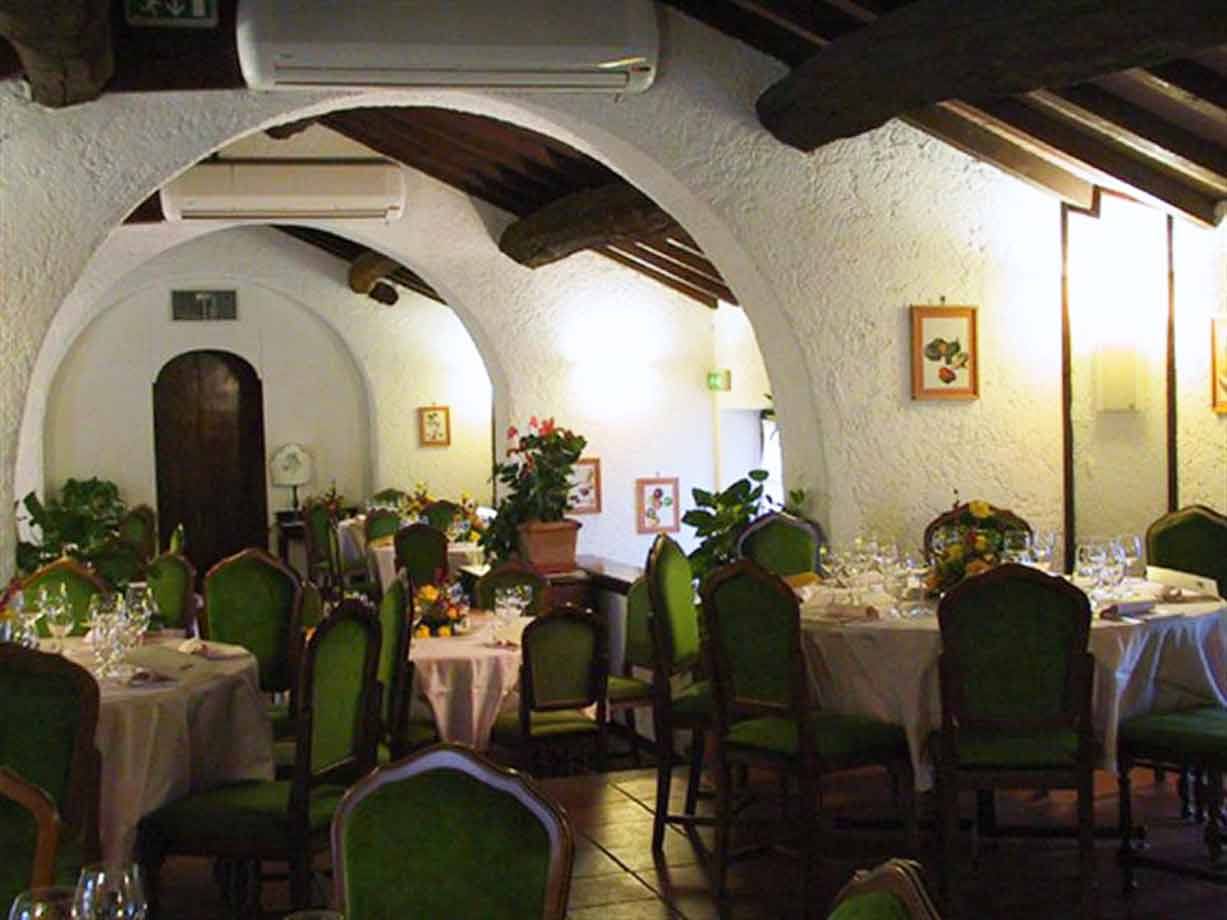 Sala ristorante con volte bianche, travi in legno e tavoli apparecchiati con sedie verdi