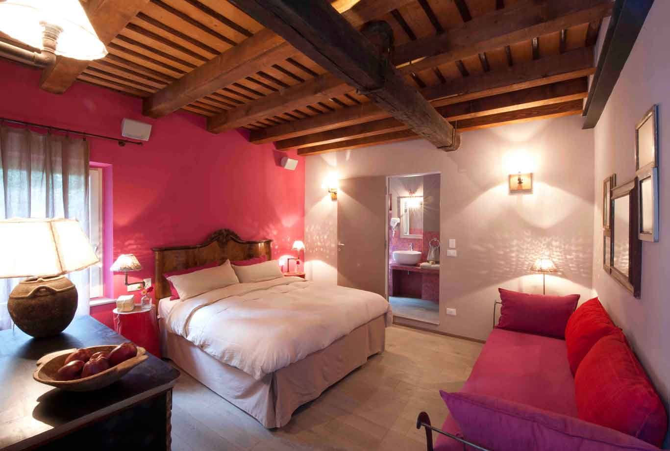 Camera d'albergo con pareti rosa, travi in legno e divano rosso