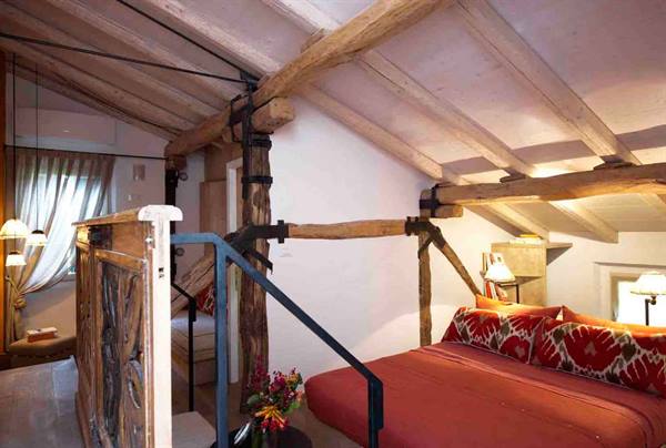 Attic bedroom with exposed wooden beams, red bed and metal staircase