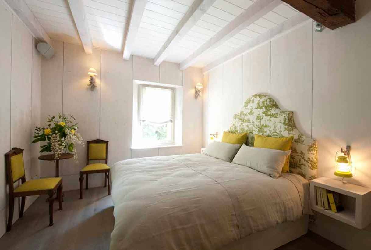 Camera da letto con travi bianche, letto matrimoniale e sedie gialle in legno