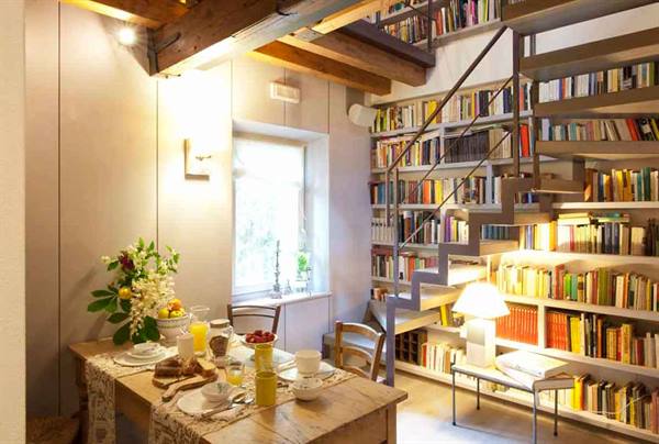 Breakfast on wooden table beside wall-to-wall bookshelf and metal staircase