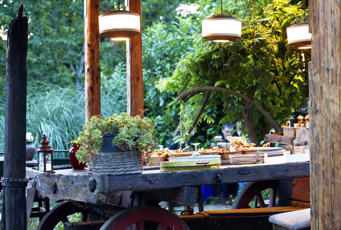 Carro di legno antico adibito a buffet, lanterne sospese e piante verdi tutt'intorno