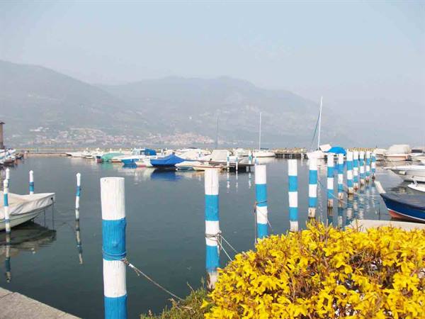 Lake marina with white and blue mooring poles, docked boats, hazy mountains