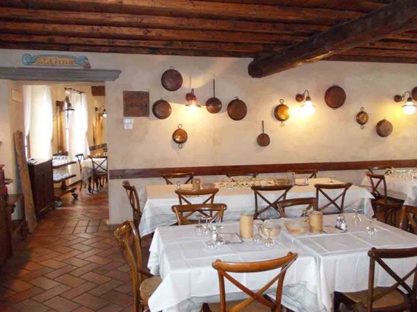 Trattoria dining room with set tables, hanging copper pans and wooden beams