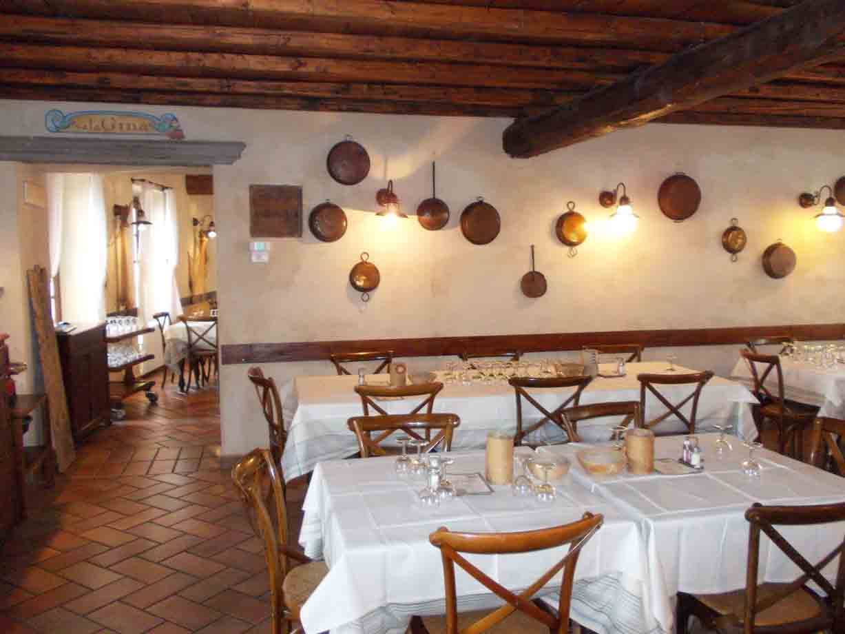 Sala di trattoria con tavoli imbanditi, padelle di rame appese e travi in legno