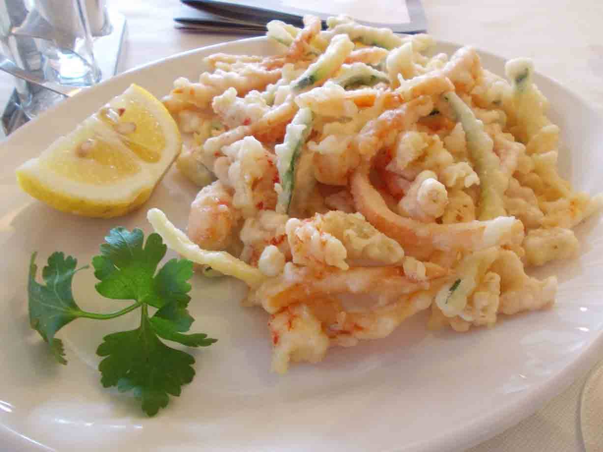 Fritto di gamberi e zucchine in pastella su piatto bianco, con limone e prezzemolo