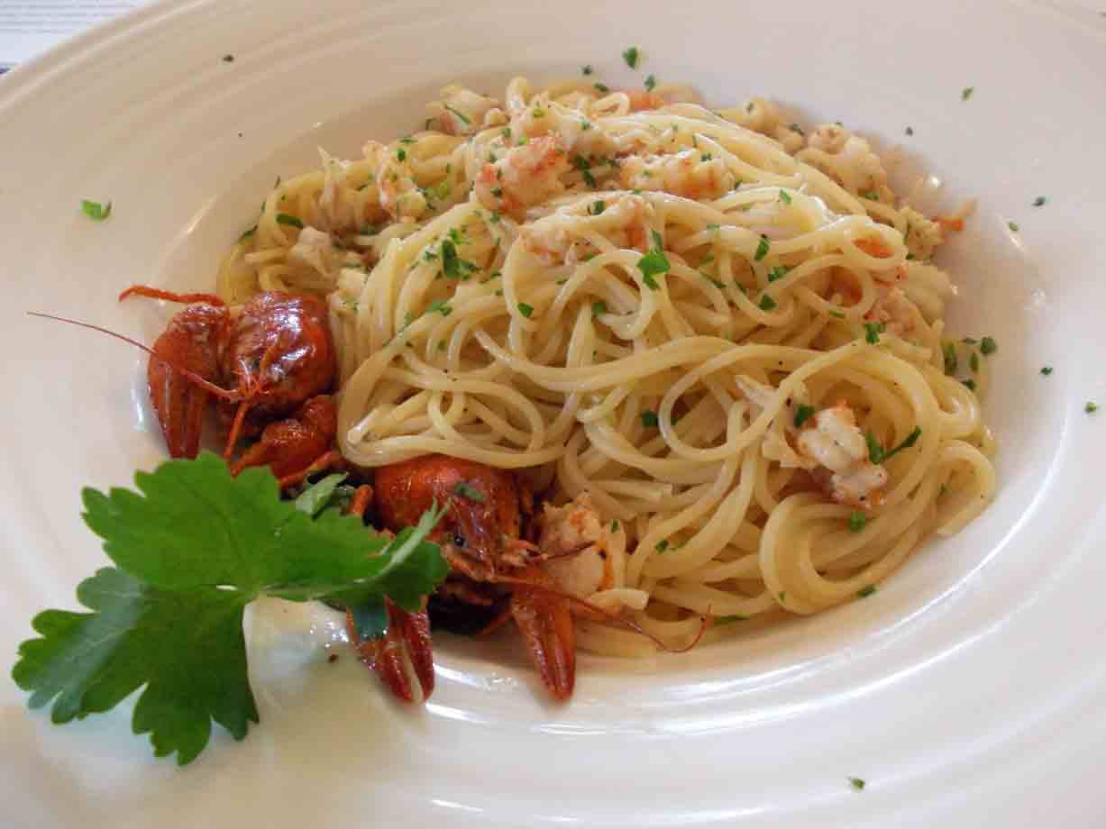 Spaghetti ai gamberetti con prezzemolo e astici interi su piatto bianco