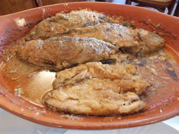 Baked fish in terracotta dish, golden sauce, indoor light