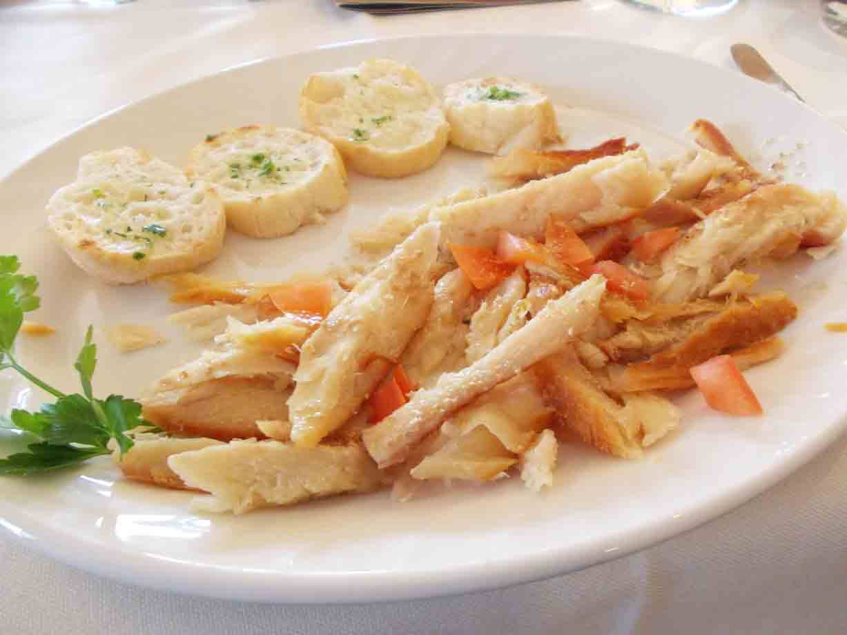 piatto bianco con baccalà sfaldato, dadini di pomodoro e crostini all'aglio
