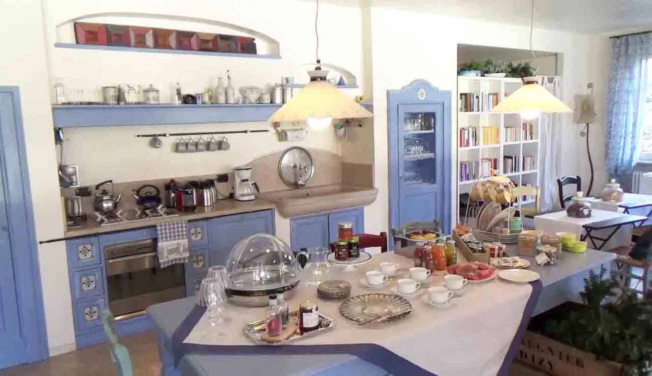 Cucina azzurra con lampadari gialli e tavolo imbandito per la colazione