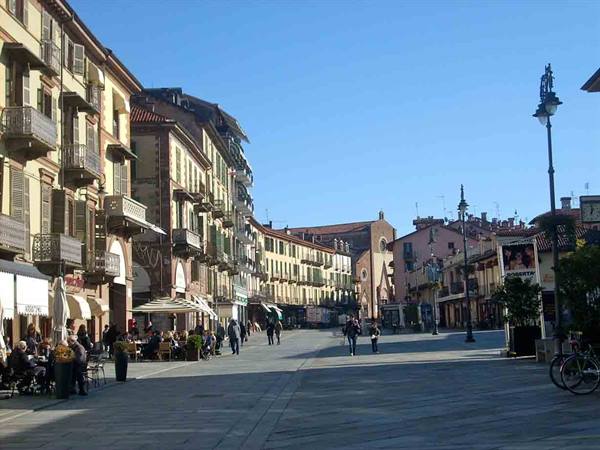 Square with arcaded buildings, cafés under umbrellas and people strolling in sunlight