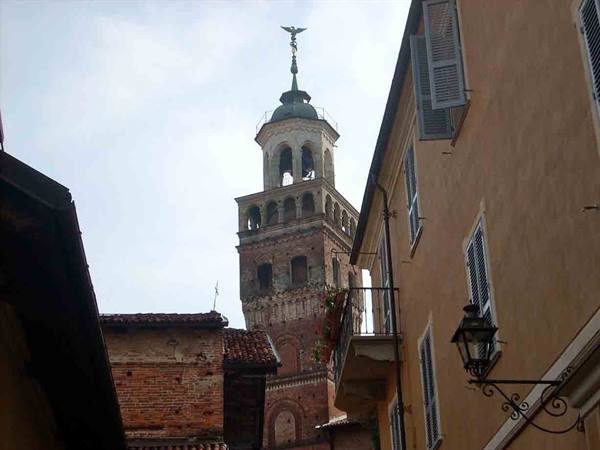 Brick bell tower between ochre houses, shuttered windows and wrought-iron street lamp