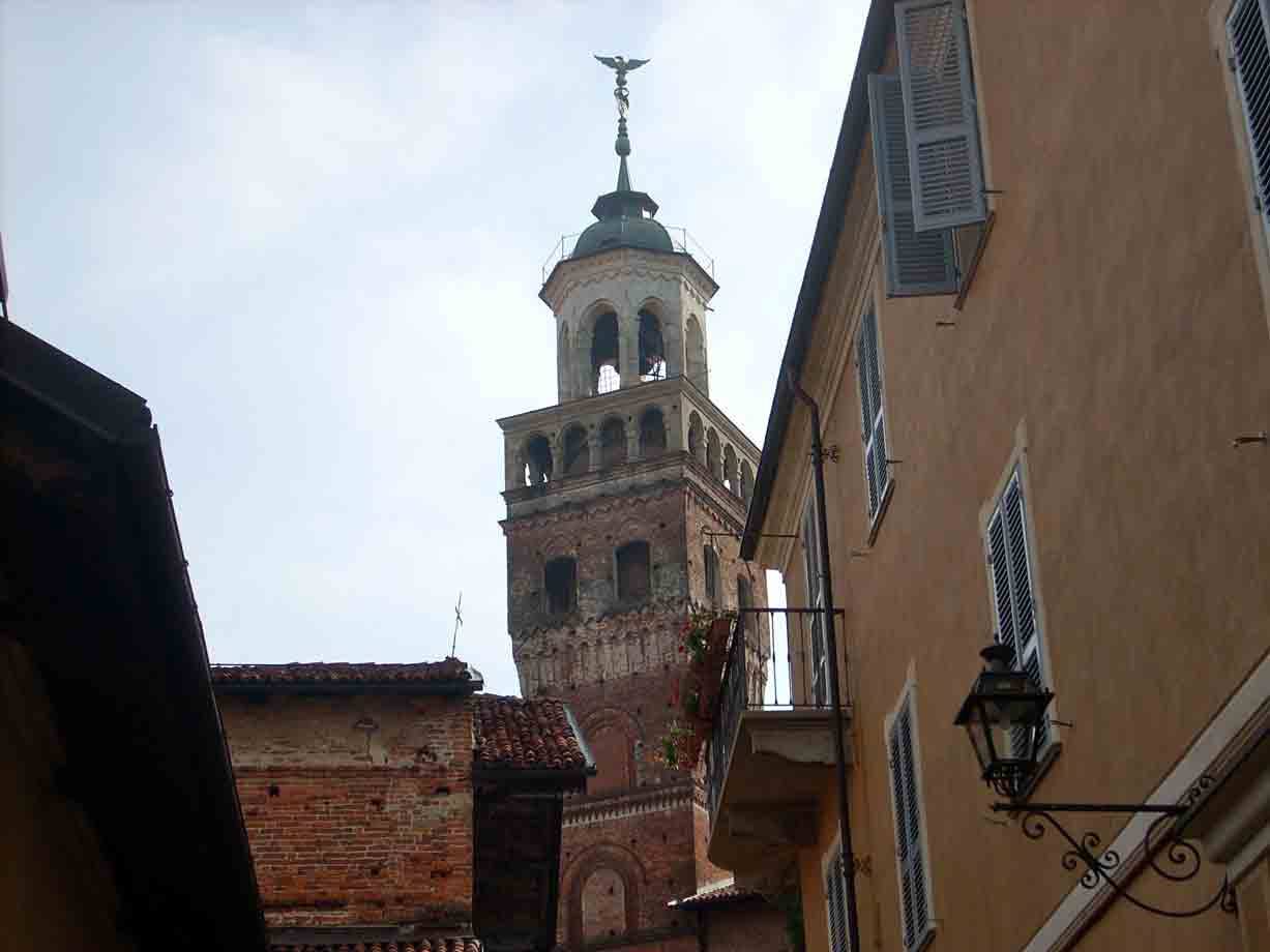 Campanile in mattoni tra case ocra, finestre con persiane e lanterna stradale