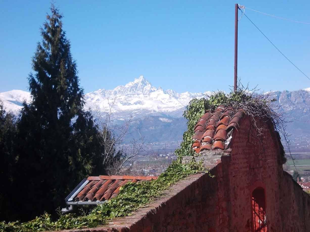 Muro di mattoni con tetti in cotto e edera, sullo sfondo il Monviso innevato