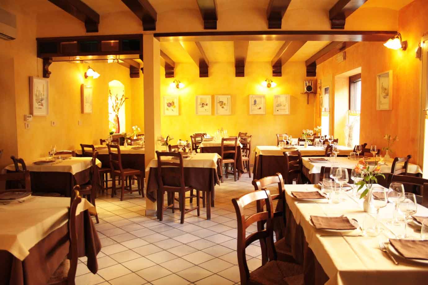 Sala di trattoria con tavoli apparecchiati, sedie in legno e travi sul soffitto