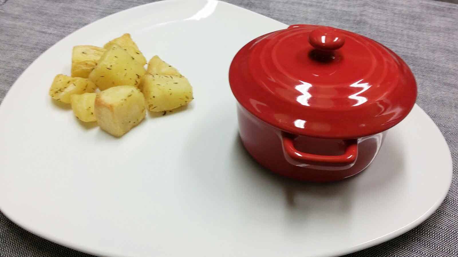 Coccetta rossa con coperchio su piatto bianco con patate lesse
