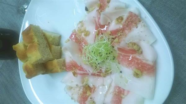 Swordfish carpaccio with sprouts and walnuts on white plate, bread beside