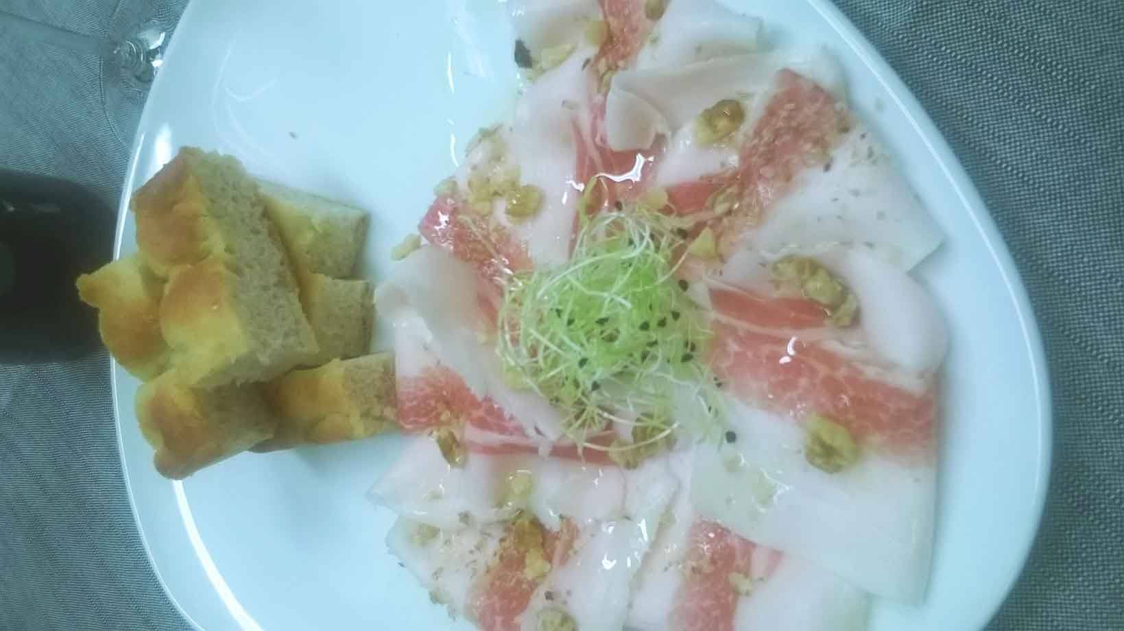 Carpaccio di pesce spada con germogli e noci su piatto bianco, pane accanto