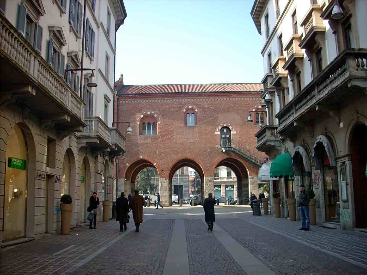 Pedoni camminano verso il Palazzo Arengario in mattoni con archi, Monza