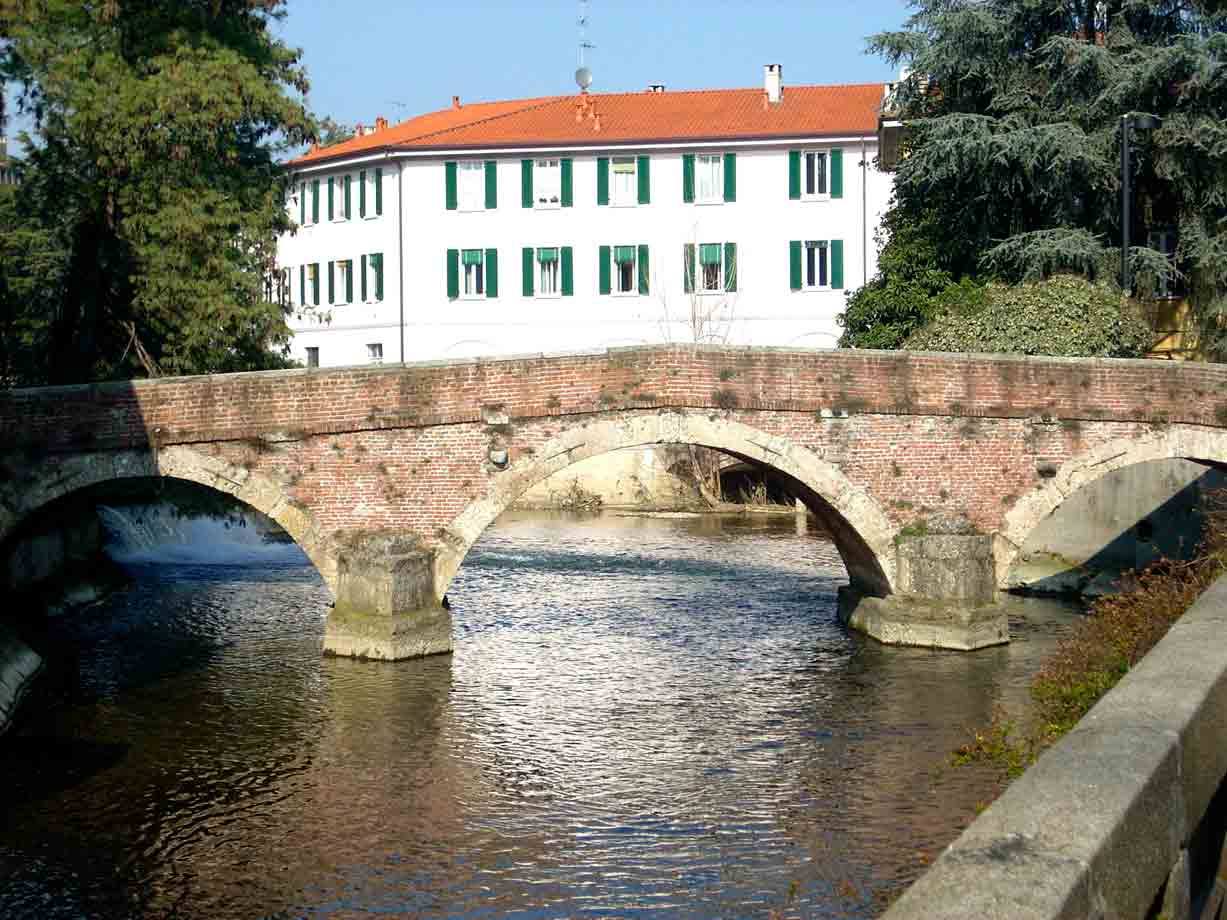 Ponte antico in mattoni con tre archi sopra un fiume, case bianche dietro