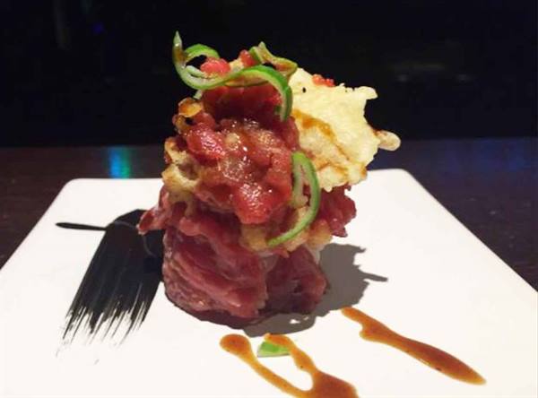 Tuna tartare with tempura and chives on white plate with sauce