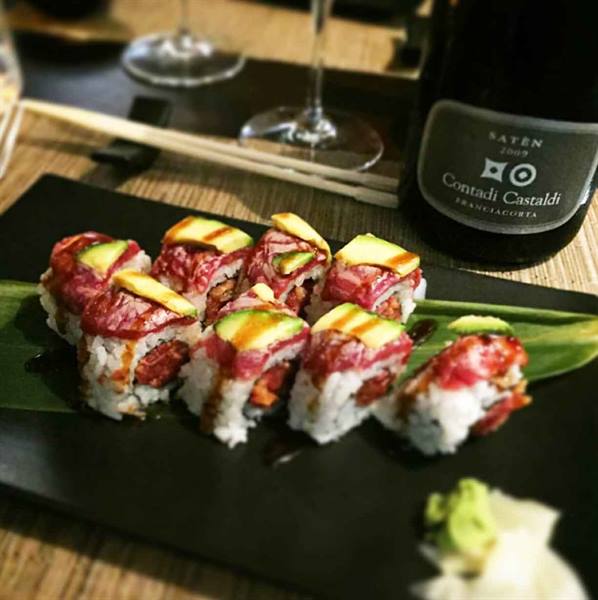 Sushi rolls with beef and avocado on black plate, beside a Franciacorta bottle