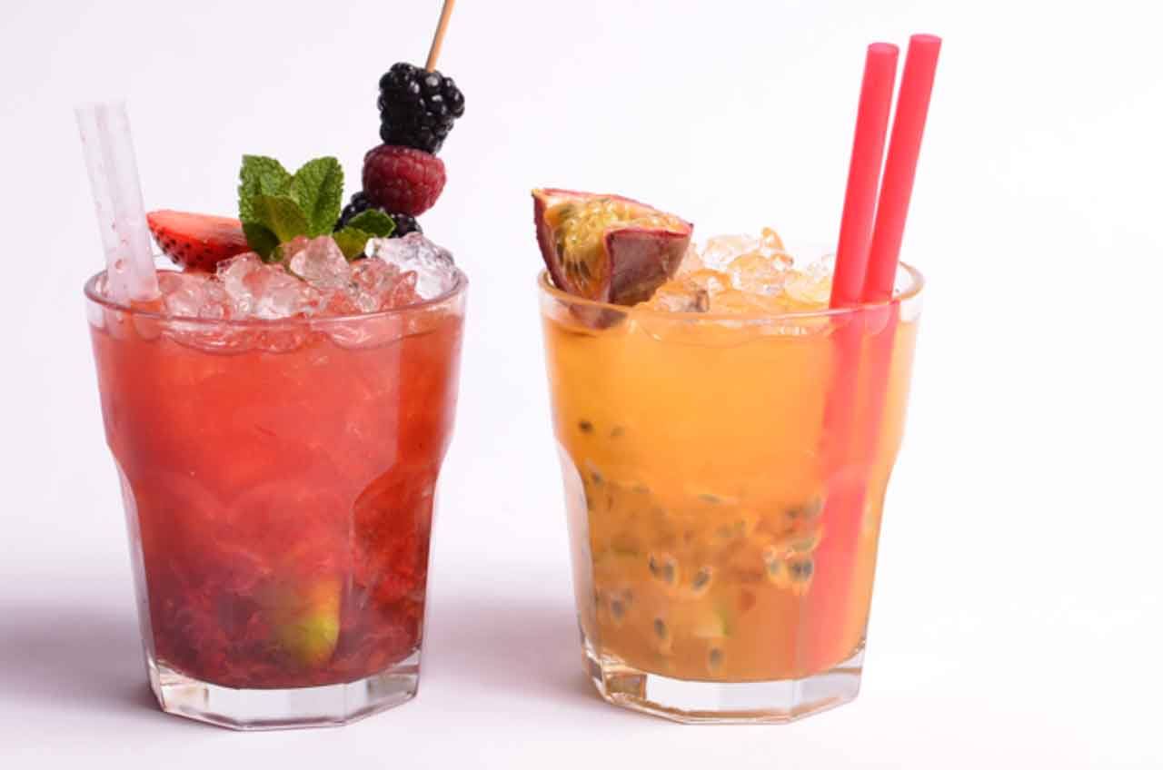 Due cocktail ghiacciati su sfondo bianco, uno ai frutti di bosco, uno al passion fruit