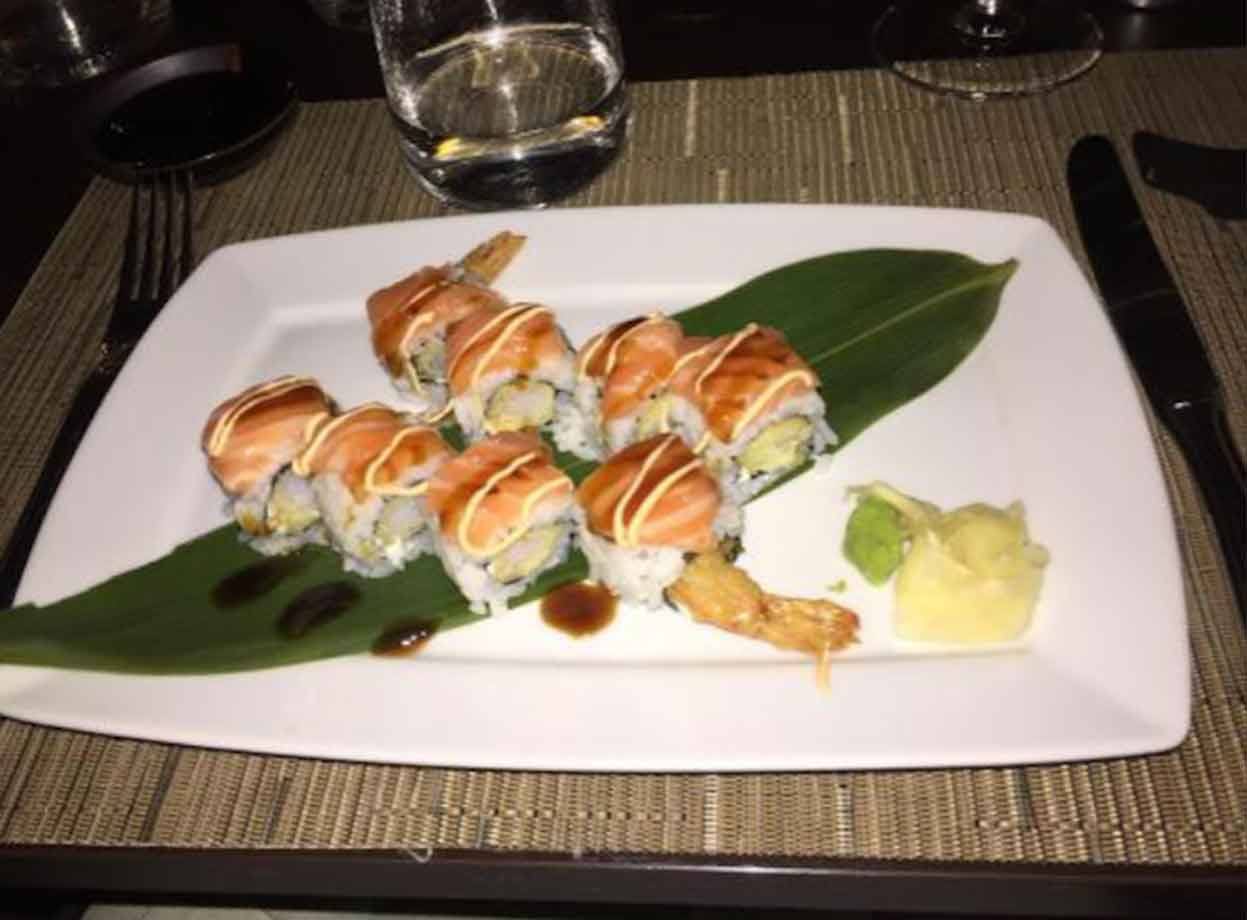 Piatti di sushi con salmone su foglia verde, posate e bicchieri in ristorante
