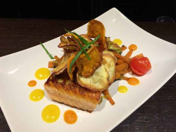 White plate with seared salmon, roasted vegetables, cherry tomato and yellow sauces