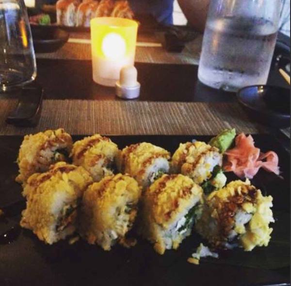 Fried sushi rolls on a black plate with ginger and wasabi, candlelight