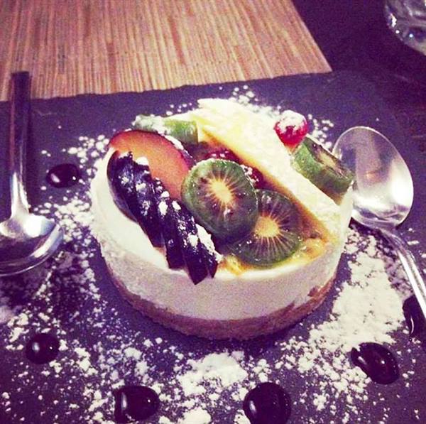 Cheesecake topped with fresh fruit and powdered sugar on slate plate