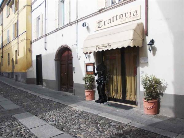 Trattoria entrance with beige awning, iron statues and potted plants, cobblestone street