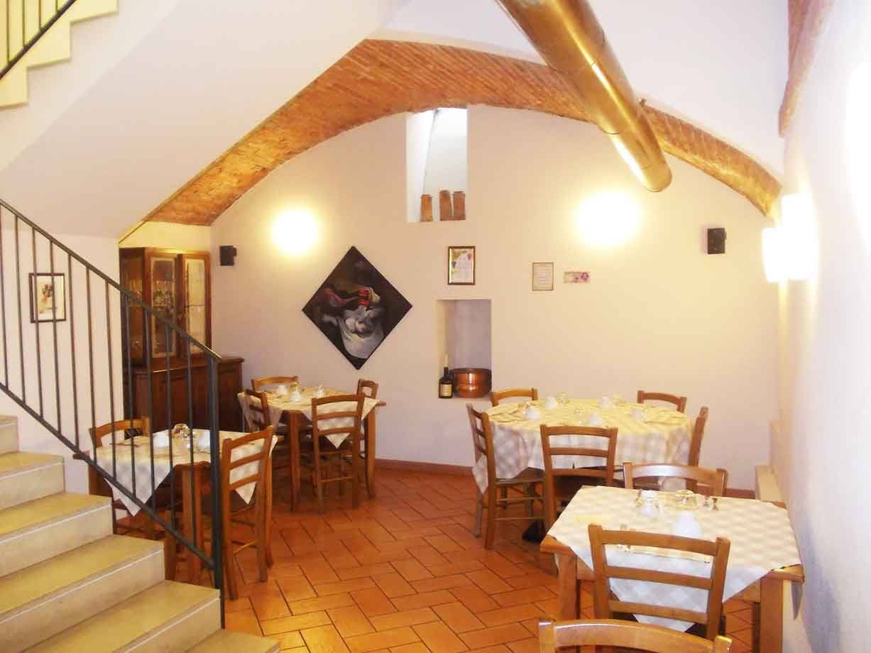 Sala di trattoria con tavoli apparecchiati, volta in mattoni e pavimento in cotto