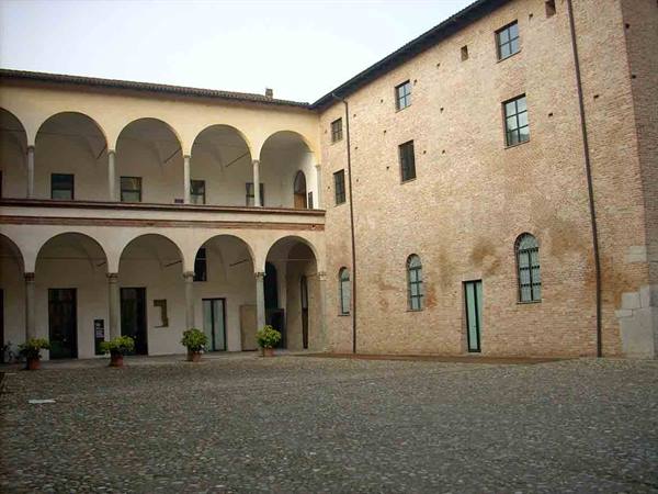 Courtyard with arched loggia, brick wall, cobblestones and potted plants