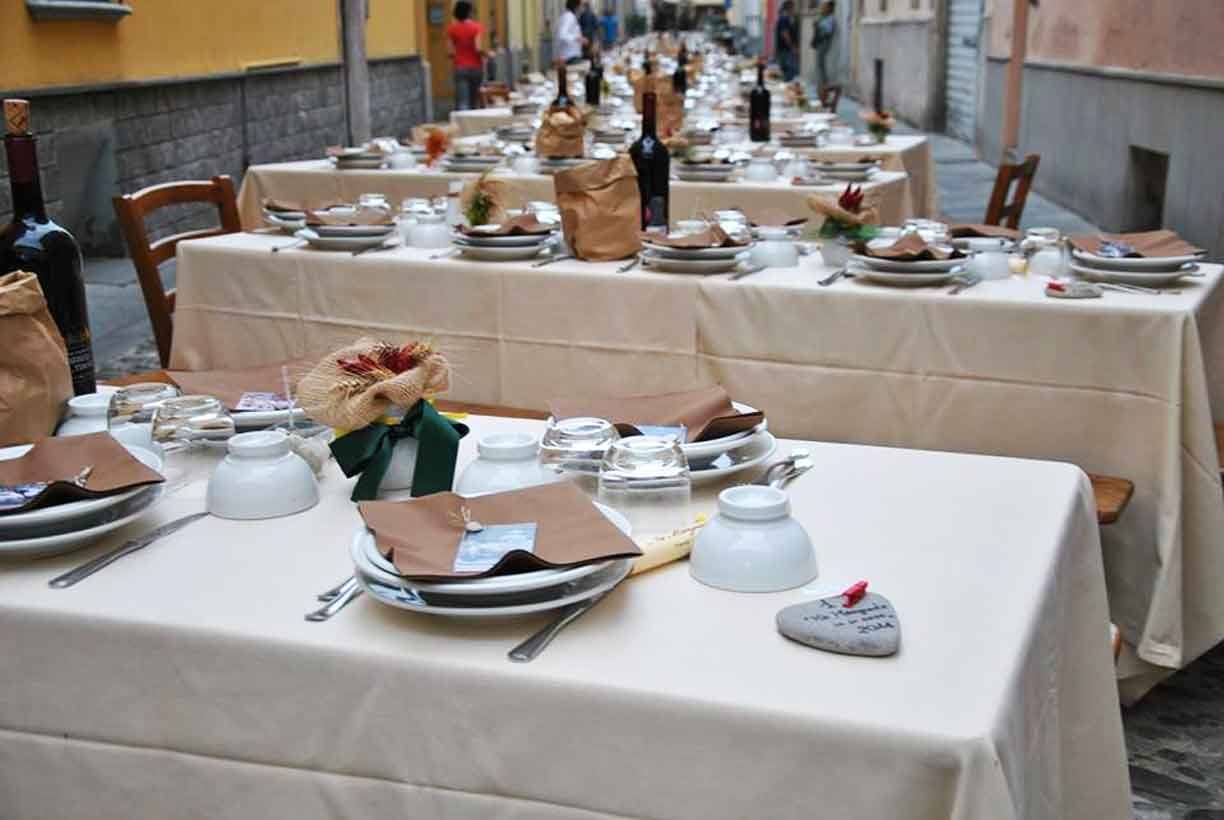 Tavole imbandite con stoviglie e bottiglie lungo un vicolo, cena all'aperto