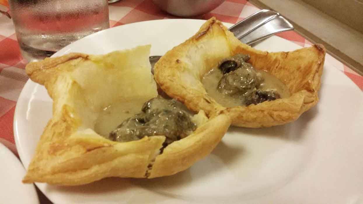 Vol-au-vent di pasta sfoglia ripieni di funghi in salsa, su piatto bianco