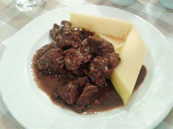White plate with beef stew in dark sauce and yellow cheese, checkered tablecloth