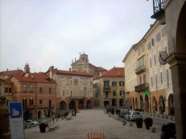 Mondovì's Piazza Maggiore: frescoed arcaded buildings, baroque church, cobblestone square under grey sky