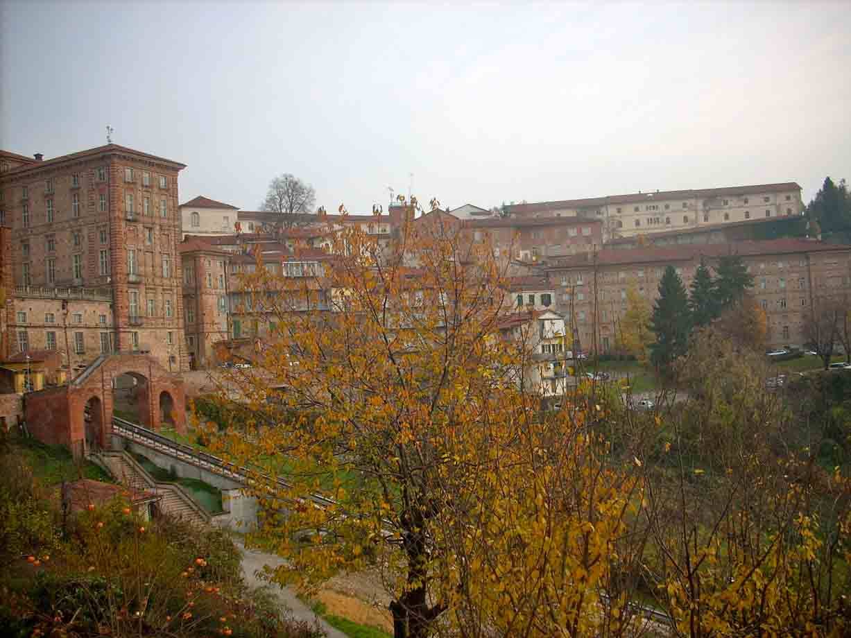 Alberi autunnali davanti ai palazzi storici in mattoni di Mondovì sotto cielo grigio