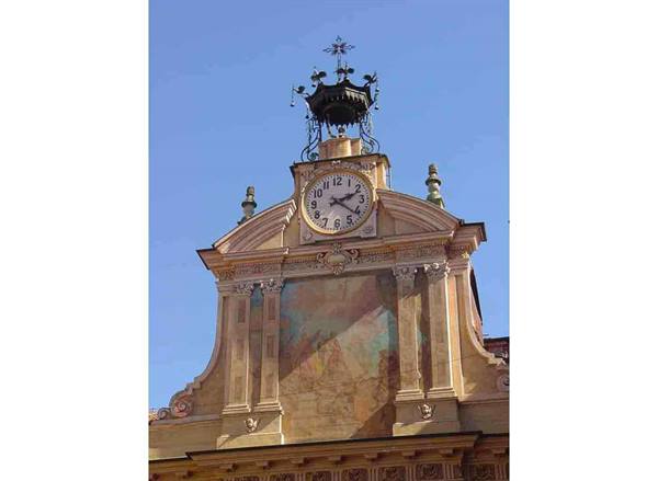 Clock on old building facade with faded fresco and wrought iron crown