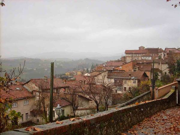 Brick rooftops over misty hills, stone wall covered with autumn leaves