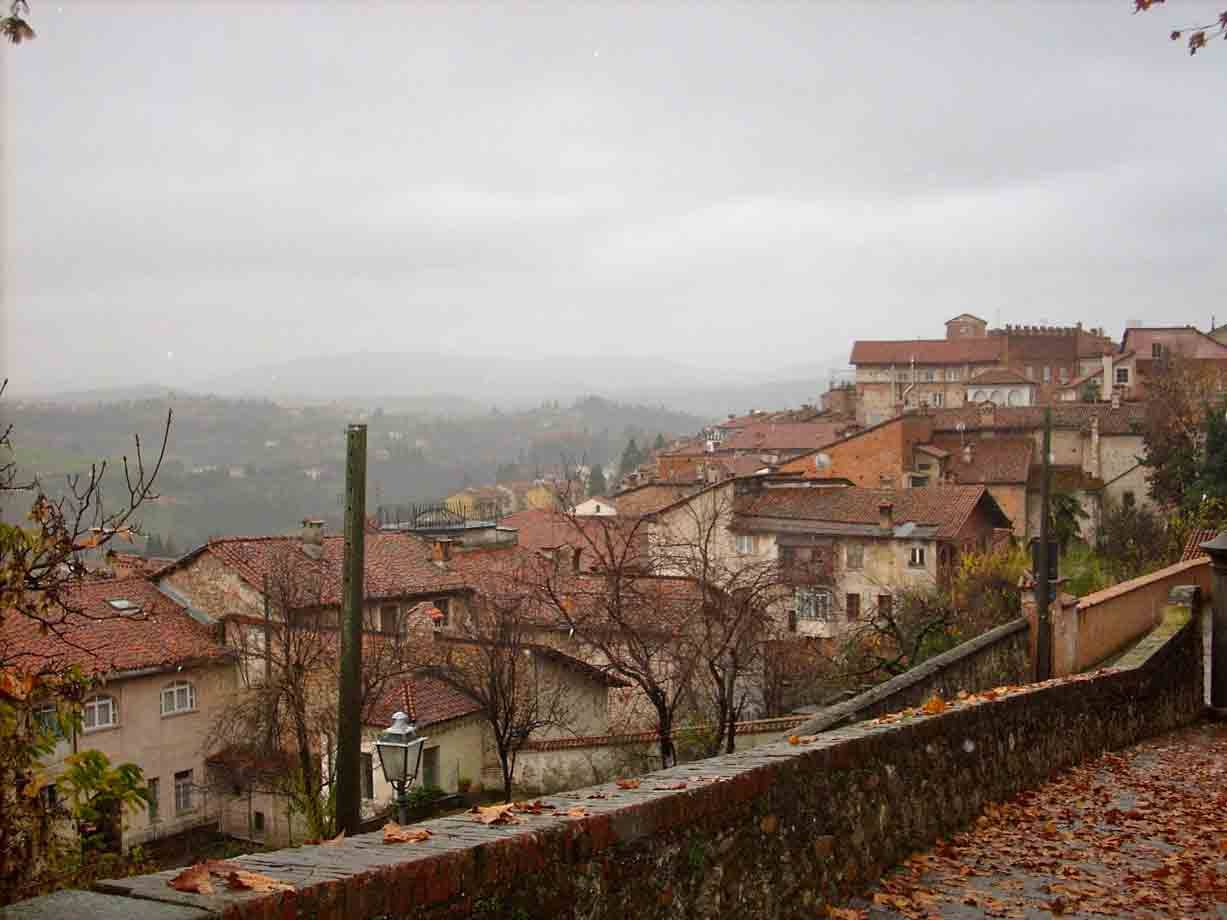 Tetti di mattoni sopra colline nebbiose, muretto di pietra con foglie autunnali