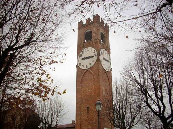 Brick clock tower among bare trees under grey sky