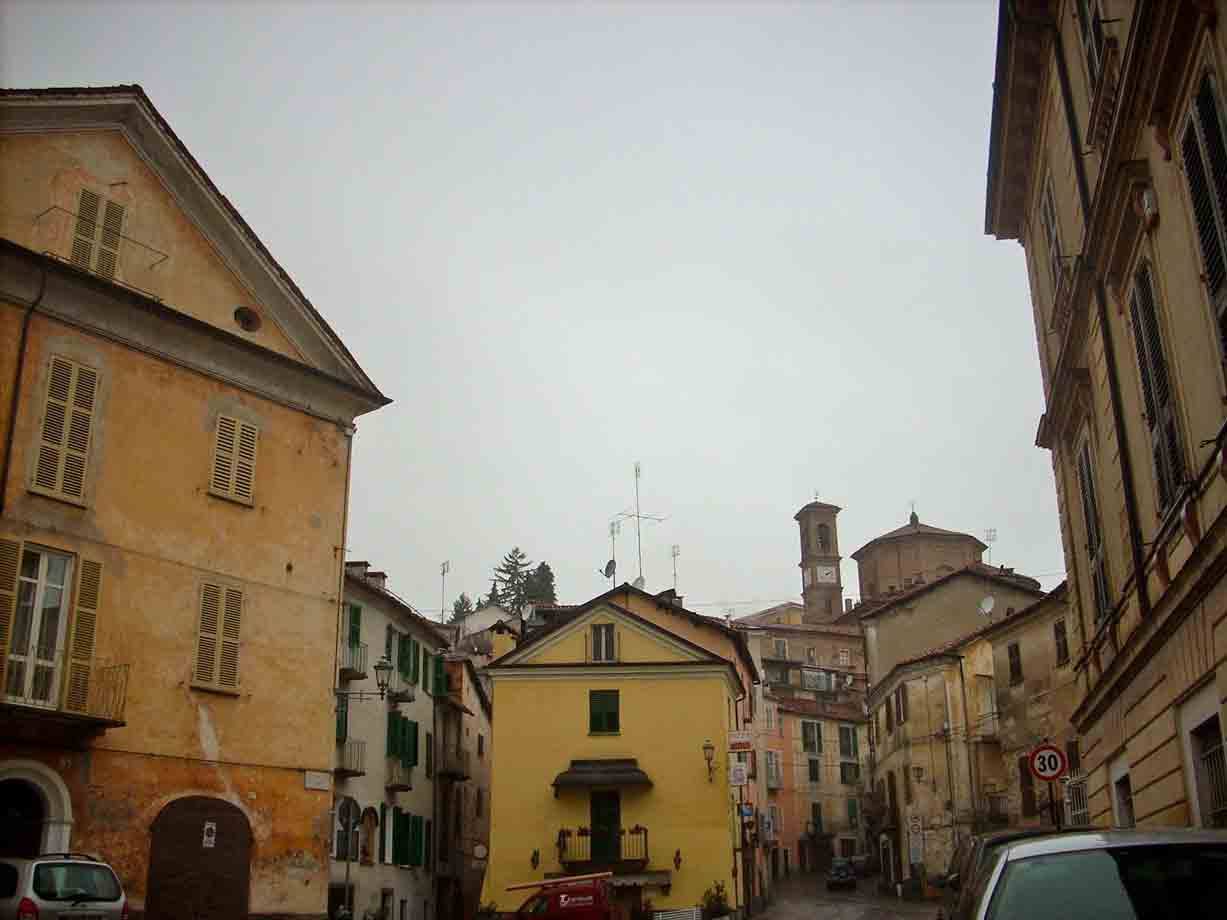 Piazza con case gialle e ocra, campanile sullo sfondo, cielo grigio