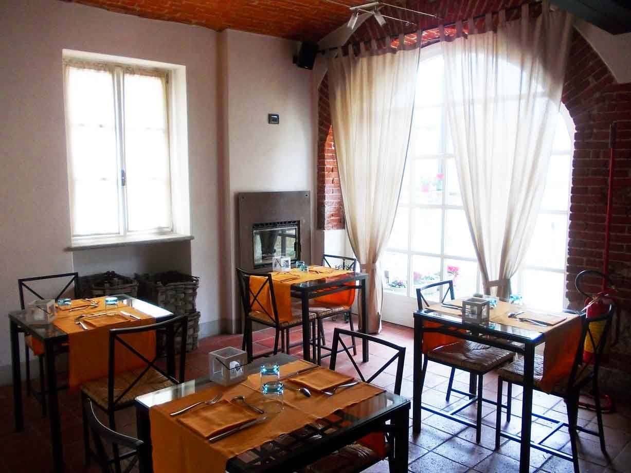 Sala di ristorante con tavoli apparecchiati, caminetto, soffitto in mattoni e tende chiare