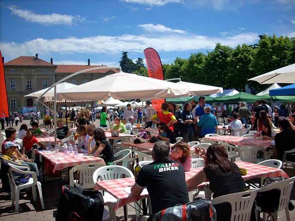 Checkered tablecloths under white umbrellas, crowd in a sunny town square