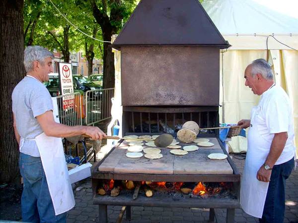 Two aproned men baking flatbreads on a wood-fired stone griddle