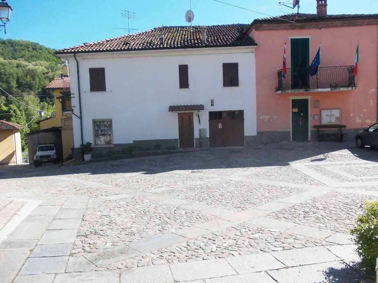 Piazzale ciottolato davanti a case colorate con bandiere e verdi colline