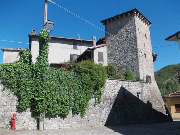 Medieval stone tower beside ivy-covered houses under clear blue sky
