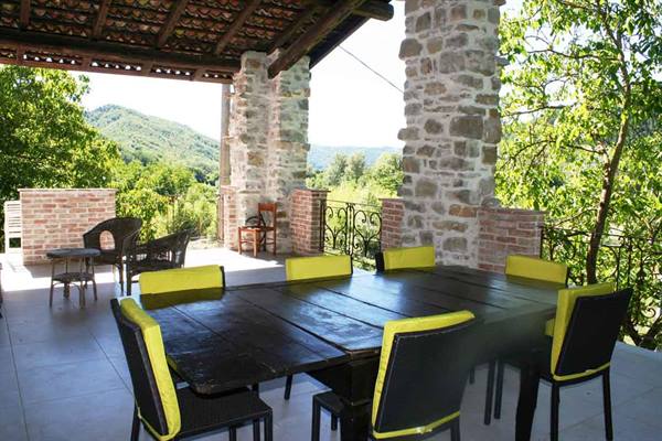 Wooden table with yellow chairs under a stone veranda, green hills